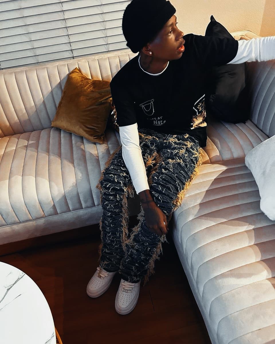 VUDU seated on a couch in a black beanie and distressed denim